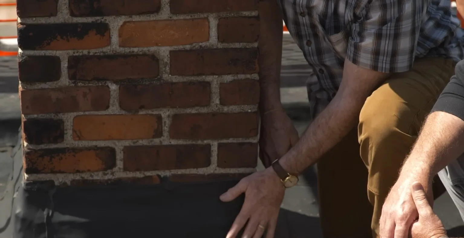 Inspecting flashing at the base of a brick chimney